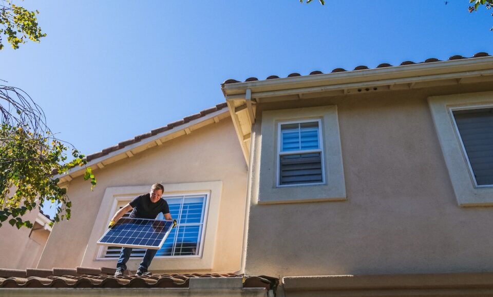 A Man Standing on the Roof while Holding a Solar Panel