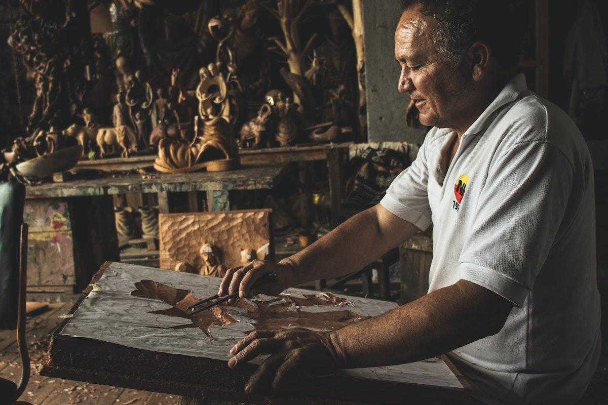 Man in White Polo Shirt Working on Wooden Sculpture